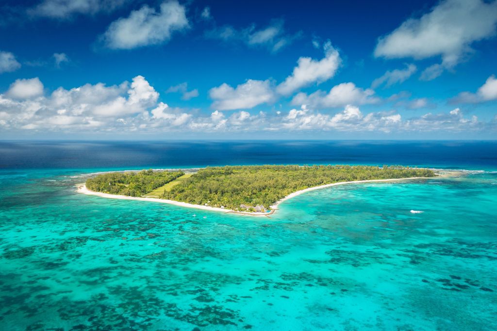 Aerial view of a tropical island surrounded by turquoise waters and a clear blue sky with white clouds.